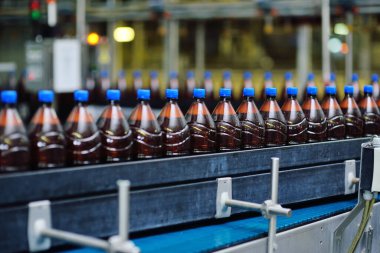 Bir bira fabrikasının arka planındaki taşıma bandındaki plastik bira şişeleri.