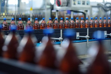 Bir bira fabrikasının arka planındaki taşıma bandındaki plastik bira şişeleri.