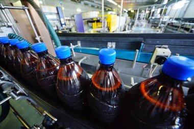 Bir bira fabrikasının arka planındaki taşıma bandındaki plastik bira şişeleri.