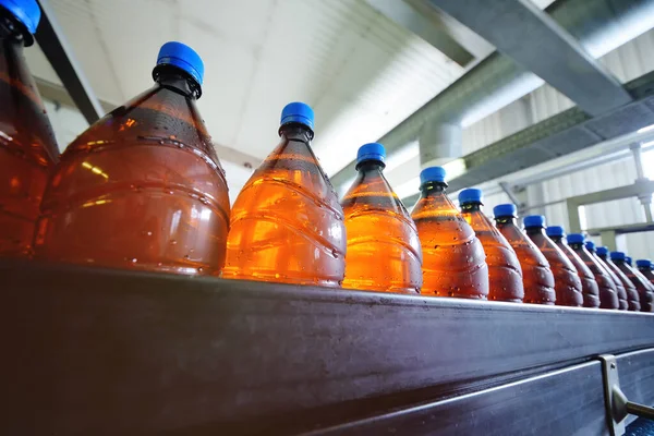 Grandi bottiglie di plastica marrone con coperchi blu con movimento birra lungo il nastro trasportatore — Foto Stock