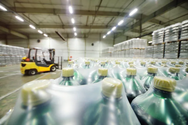 Cargador en el fondo de un enorme almacén industrial de alimentos con botellas de plástico PET con cerveza, agua, bebidas. —  Fotos de Stock