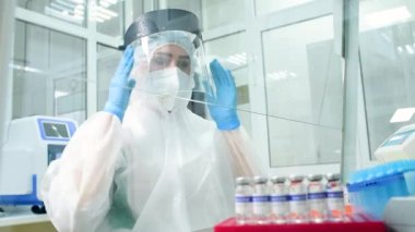 Koruyucu kıyafetli bir araştırmacı mikrobiyolog PCR laboratuvarında çalışmaya başlamadan önce koruyucu bir kask takıyor.