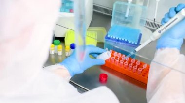 Koruyucu giysi giymiş, steril maske takan, kasklı, elinde şeker kutusuyla lastik eldivenli kadın PCR laboratuvar araştırmacısı.