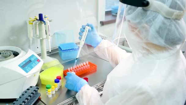 Γυναίκα ερευνήτρια εργαστηρίου PCR με προστατευτική ιατρική στολή, αποστειρωμένη μάσκα, κράνος, λαστιχένια γάντια με ένα διανομέα στα χέρια της — Αρχείο Βίντεο