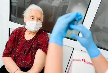 Lastik eldiven giyen bir doktor yaşlı bir kadına hastanede iğne yapmaya hazırlanıyor..