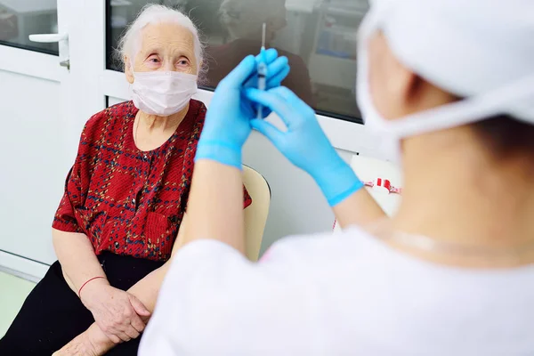 Médico vestindo luvas de borracha se prepara para injetar uma mulher idosa no hospital. — Fotografia de Stock