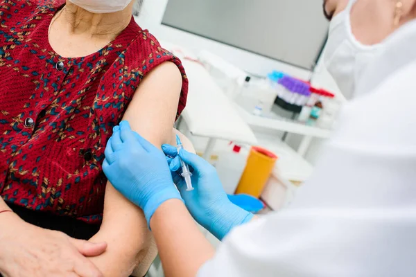 La enfermera que usa una máscara médica y guantes de goma está inyectando o inyectando una vacuna contra el virus en el hombro de una mujer anciana — Foto de Stock