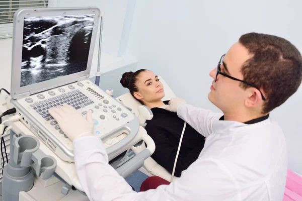Médico realiza um exame de ultra-som da glândula tireóide de uma mulher jovem e bonita em uma clínica moderna. Prevenção do cancro da tiróide. — Fotografia de Stock