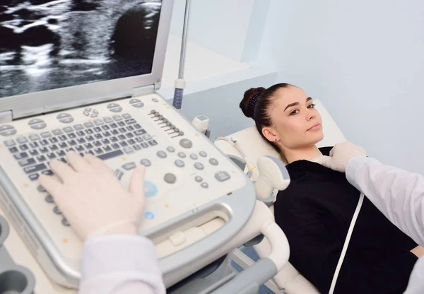 Orvos egy modern diagnosztikai klinikán vizsgálja a pajzsmirigy egy beteg egy fiatal vonzó nő egy ultrahang gép — Stock Fotó