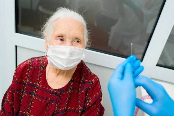 Un médico que usa guantes de goma se prepara para inyectar a una mujer mayor en el hospital. Fotos De Stock Sin Royalties Gratis