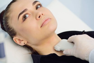 Modern bir teşhis kliniğinde doktor, ultrason makinesinde genç ve çekici bir kadının tiroit bezini inceler.