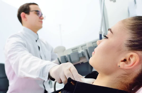 Médico en una clínica de diagnóstico moderno examina la glándula tiroides de un paciente de una mujer joven atractiva en una máquina de ultrasonido —  Fotos de Stock