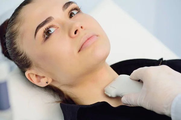 Médico en una clínica de diagnóstico moderno examina la glándula tiroides de un paciente de una mujer joven atractiva en una máquina de ultrasonido — Foto de Stock