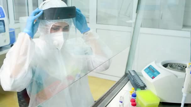 Мікробіолог у захисному костюмі одягає захисний шолом перед початком роботи в лабораторії ПЛР. — стокове відео