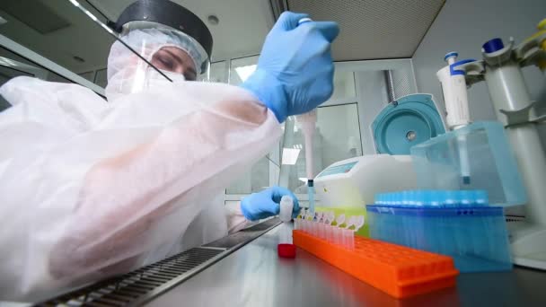 Koruyucu giysi giymiş, steril maske takan, kasklı, elinde şeker kutusuyla lastik eldivenli kadın PCR laboratuvar araştırmacısı. — Stok video