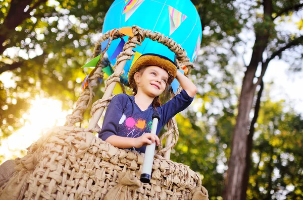 Uma menina bonita em um chapéu de palha está sorrindo em uma cesta de balão. — Fotografia de Stock