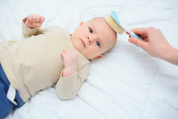 Mãe penteia o bebê com uma escova de cabelo especial em um fundo branco. — Fotografia de Stock