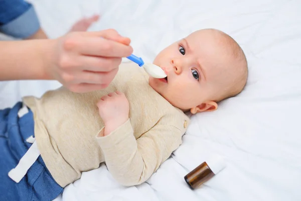 Matka dává dítěti dětský sirup z malé lžíce na bílém pozadí a na pozadí láhve léku. — Stock fotografie