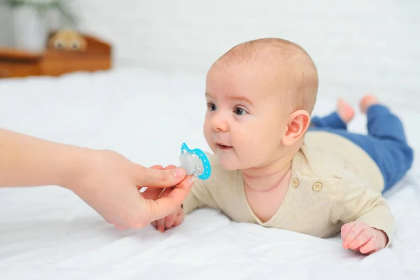 Main donne une sucette à son bébé fils sur un fond blanc. — Photo