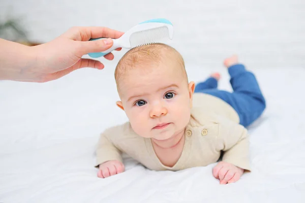 Mãe penteia o bebê com uma escova de cabelo especial em um fundo branco. — Fotografia de Stock