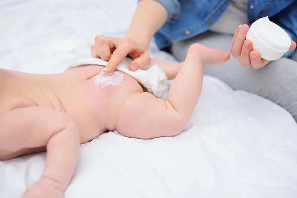 Mothers hand applies a moisturizing baby cream to the baby boys skin. Hygiene of the newborn child. — Stock Photo, Image