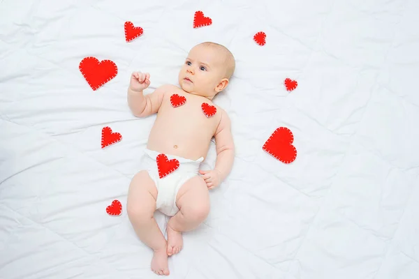 Chlapeček v bílé plence leží na pozadí červených srdcí. Láska, Valentýn — Stock fotografie