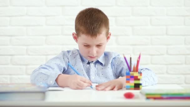 Skolpojke skriver i en anteckningsbok sitter vid ett vitt bord. — Stockvideo