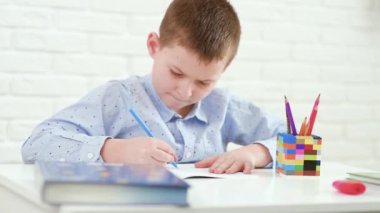Okul çocuğu beyaz bir masada oturan bir deftere yazıyor..