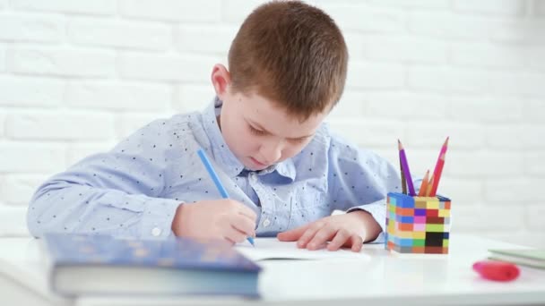 Κουρασμένος από τις σχολικές δραστηριότητες, το παιδί αγόρι γράφει σε ένα σημειωματάριο και ξαπλώνει για να ξεκουραστεί στο τραπέζι. — Αρχείο Βίντεο