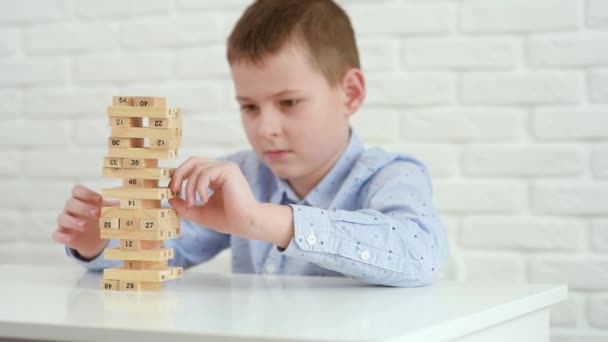 Dítě chlapec staví věž z dřevěných bloků sedí u bílého stolu. — Stock video