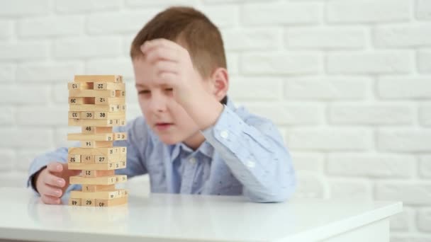 Niño niño construye una torre de bloques de madera sentado en una mesa blanca. — Vídeo de stock