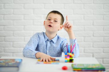 Beyaz bir masada oturan gözlüklü bir çocuk bir jest gösterir. İşaret parmağı..