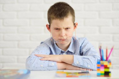 Beyaz bir masada oturan gözlüklü çocuk, defterler, kitaplar ve kalemlerden oluşan bir arka plana alınmıştı..