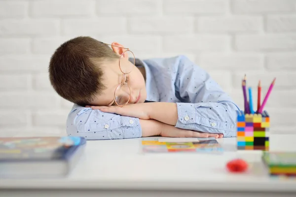 Anak sekolah lelah belajar tidur duduk di mejanya berlawanan dengan latar belakang buku dan buku catatan — Stok Foto