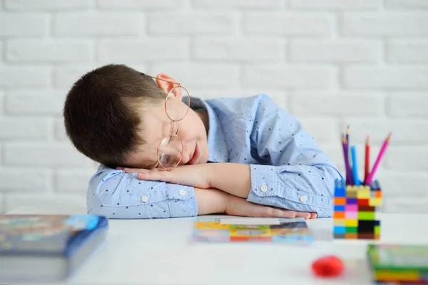 Anak sekolah lelah belajar tidur duduk di mejanya berlawanan dengan latar belakang buku dan buku catatan — Stok Foto