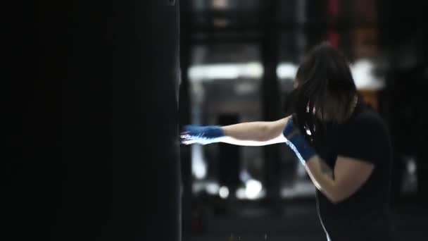 Young female boxer wraps bandages around her arms and hits a punching bag. — Stock Video