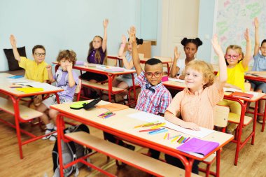 Küçük çocuklar okul çocukları gülümser ve bir bayan öğretmenin ve bir okul sınıfının geçmişine tepki vermek için ellerini kaldırırlar. Okula geri dön.