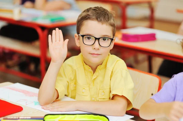 Niño pequeño colegial con una camisa y gafas amarillas busca una respuesta en el fondo de un aula de escuela primaria. Regreso a la escuela. — Foto de Stock