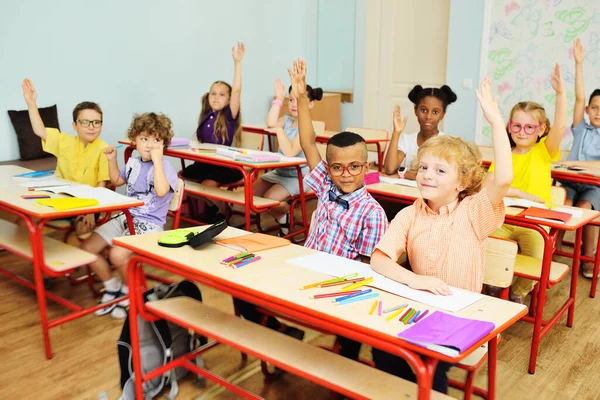 Anak-anak sekolah kecil tersenyum dan mengangkat tangan mereka untuk menanggapi latar belakang seorang guru perempuan dan kelas sekolah. Kembali ke sekolah — Stok Foto