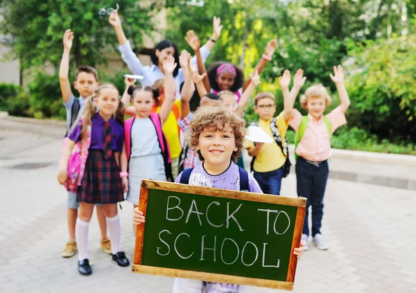 Anak sekolah dengan rambut keriting di latar belakang sekelompok anak-anak teman sekelas memegang tanda dengan tulisan "kembali ke sekolah." — Stok Foto