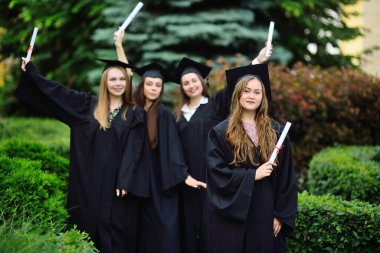 Genç bir kız, siyah cüppeli bir üniversite mezunu ve elinde diploması olan kare bir şapkayla sınıf arkadaşlarının geçmişine gülümsüyor..