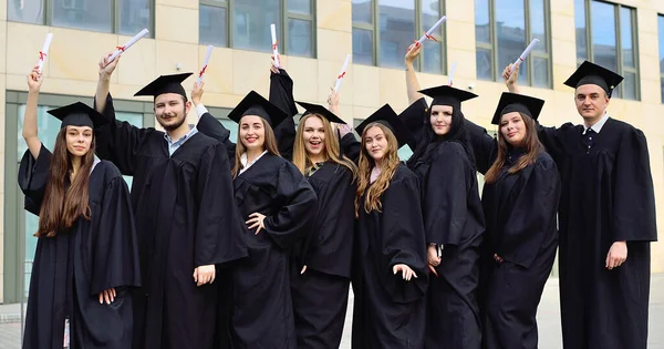 Absolventinnen und Absolventen in schwarzen Studentenkleidern und quadratischen Hüten freuen sich über Diplome und beenden den Bildungsprozess. — Stockfoto