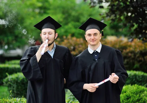 Siyah cübbeli ve kare şapkalı bir erkek öğrenci diplomasını ya da sertifikasını içiyor. Esrar, esrar ve öğrenci hayatı. — Stok fotoğraf