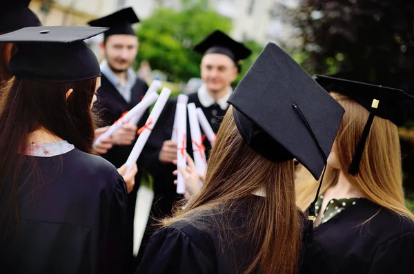 Groep van universitaire afgestudeerden in student gewaden of mantel en vierkante hoeden bij de diploma-uitreiking houden college diploma diploma 's in hun handen en verheugen zich. — Stockfoto