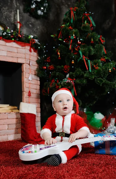 Niño vestido como Papá Noel sentado con una guitarra en su han —  Fotos de Stock