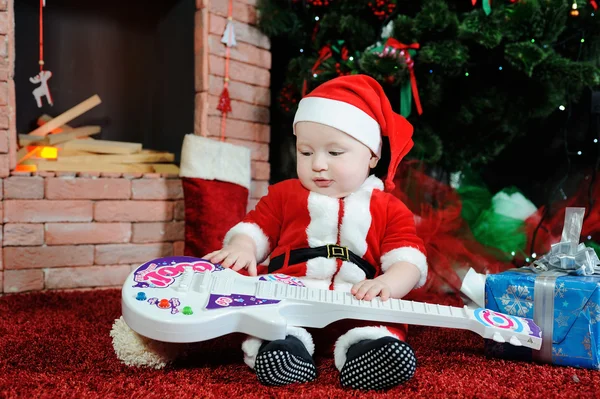 Niño vestido como Papá Noel sentado con una guitarra en su han —  Fotos de Stock