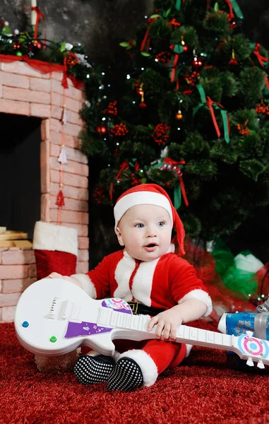 Niño vestido como Papá Noel sentado con una guitarra en su han —  Fotos de Stock