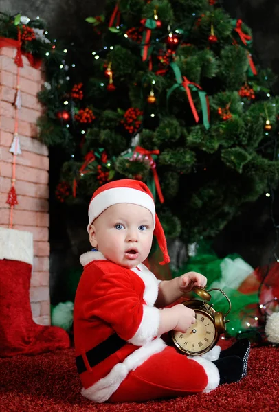 Baby boy dressed as Santa Claus sits on the red carpet on the ba — Stock Photo, Image