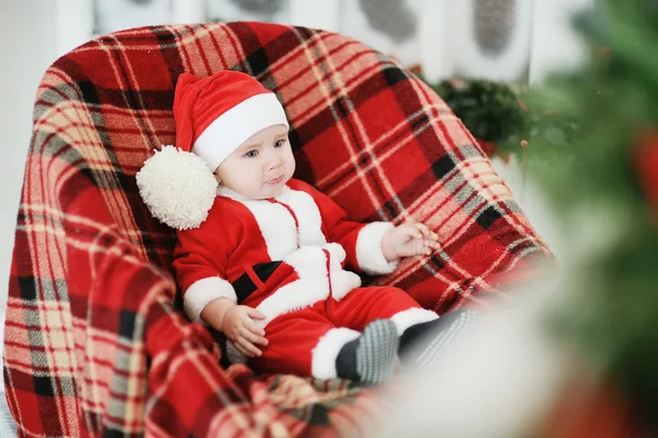 Child dressed as Santa Claus sits in a plaid chair — Stock Image Child dressed as Santa Claus sits in a plaid chair Stock Photo