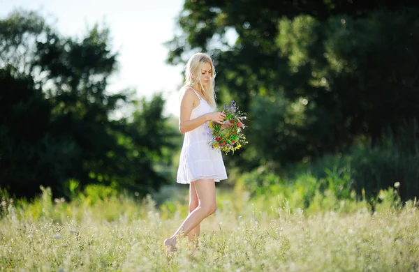 Meisje in een witte sundress en met een krans van bloemen in de hand op — Stockfoto